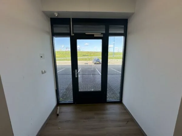 Kleine entree met glazen deur aan de Van der Hagenstraat met uitzicht op een parkeerplaats en dijk.